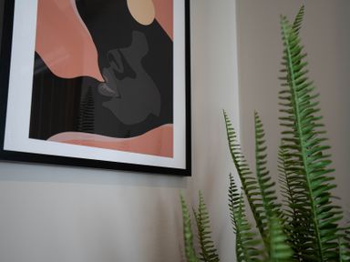 A framed abstract art piece on a wall next to green fern leaves at The Reef in Kessingland