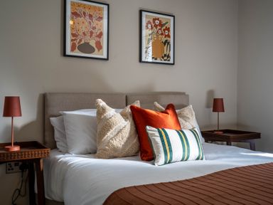 A bedroom with a bed with pillows and two bedside tables with lamps and two framed artworks at The Reef in Kessingland