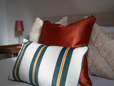 Decorative pillows on a bed with a bedside table and lamp in the background at The Reef in Kessingland