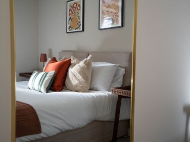 A bedroom with a bed made with white sheets and several pillows next to a nightstand and two framed pictures on the wall
