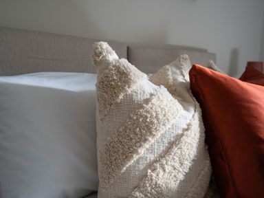 A bed with textured beige and solid rust colored pillows at The Reef in Kessingland