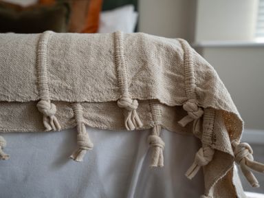 A beige woven blanket with knotted tassels draped over a white bed at The Reef in Kessingland
