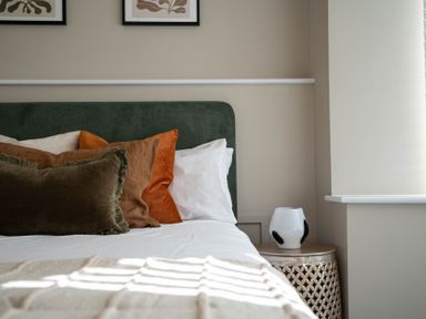 A bed with multiple pillows and a side table with a vase in a bedroom at The Reef in Kessingland