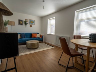 A living room with a blue sofa a round coffee table a dining table with brown chairs and wall decorations at The Cove in Kessingland