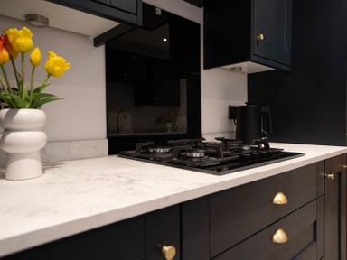A kitchen countertop with a gas stove a black kettle and a vase with yellow tulips at The Cove in Kessingland