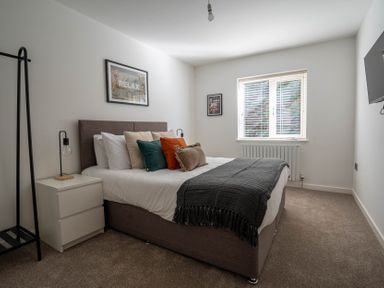 A bedroom with a bed pillows a bedside table lamps window and a wall-mounted tv at The Cove in Kessingland