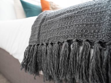 A close up of a textured gray throw with tassels on a bed with pillows at The Cove in Kessingland