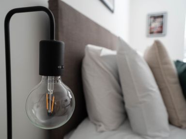 A close up of a light bulb on a lamp next to a bed with pillows