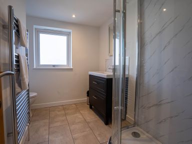 A bathroom with a shower enclosure sink vanity unit towel radiator and tiled floor at The Cove in Kessingland
