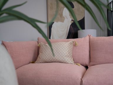 A pink sofa with a patterned cushion a lamp and a painting in the background at Coral Cottage in Kessingland