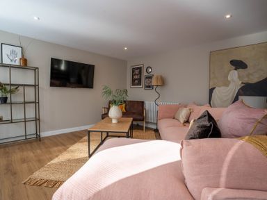 A living room with a pink sofa a wooden coffee table and a wall-mounted tv at Coral Cottage in Kessingland