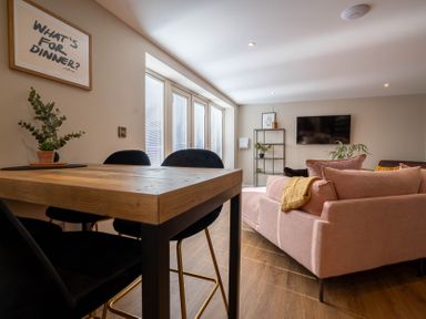 A dining table with black chairs and a pink sofa in a living room at Coral Cottage in Kessingland