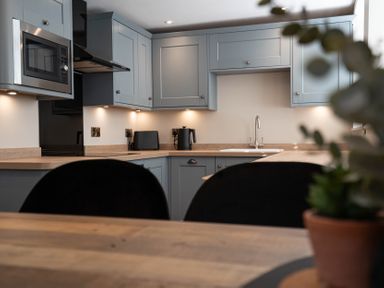 A kitchen with blue cabinets wooden countertops a microwave kettle and a toaster at Coral Cottage in Kessingland