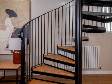 A spiral staircase with wooden steps beside a table with a lamp and a painting on the wall at Coral Cottage in Kessingland