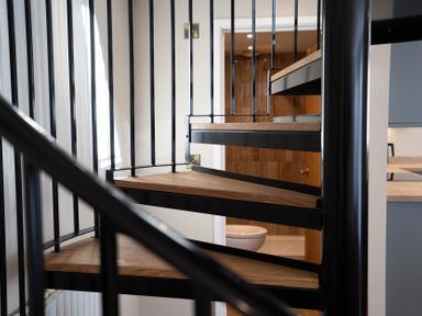 A spiral staircase with wooden steps and black metal railings inside a home at Coral Cottage in Kessingland