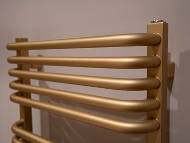 A close up of a gold colored wall mounted heated towel rail at Coral Cottage in Kessingland