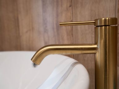 A brass faucet above a white sink with wooden paneling in the background at Coral Cottage in Kessingland