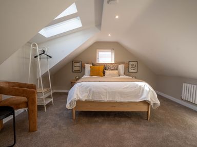 A bedroom with a bed and pillows under a skylight with a chair and a clothes rack at Coral Cottage in Kessingland