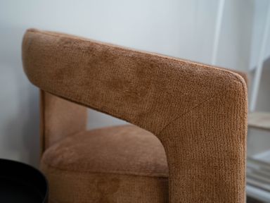 A close up of a brown upholstered chair with a circular seat and curved backrest at Coral Cottage in Kessingland
