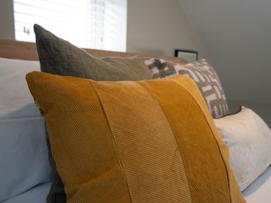 A close up of mustard and gray cushions on a bed with a window in the background at Coral Cottage in Kessingland
