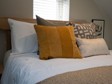 A bed with white sheets and multiple pillows including an orange one at Coral Cottage in Kessingland