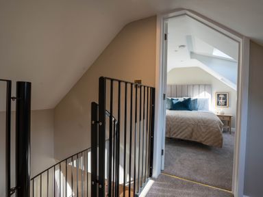 A staircase with black metal railing leading to a bedroom with a bed and side table at Coral Cottage in Kessingland