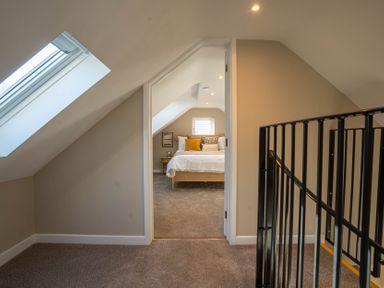 A hallway with a skylight window and black railing leading to a bedroom with a bed and pillows at Coral Cottage in Kessingland