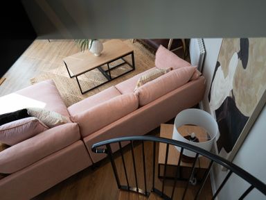 A living room with a pink sofa, a wooden coffee table, a rug, a side table with a lamp, and abstract wall art at Coral Cottage in Kessingland