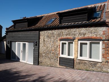Exterior of a building with cobblestone and dark wood panel walls with windows and double glass doors at Coral Cottage in Kessingland