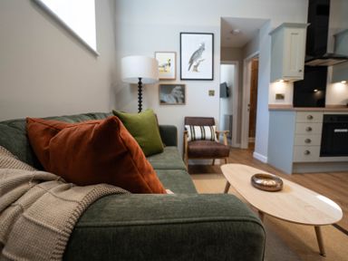 A living room with a green sofa and colorful pillows a wooden coffee table and a chair at Dunes Cottage in Kessingland