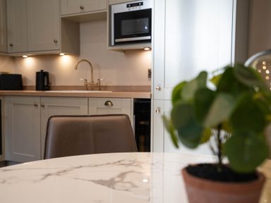 A kitchen with beige cabinets a brass faucet a microwave and a plant on a marble table at Dunes Cottage in Kessingland