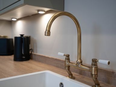 A kitchen sink with a brass faucet on a wooden countertop and black appliances at Dunes Cottage in Kessingland