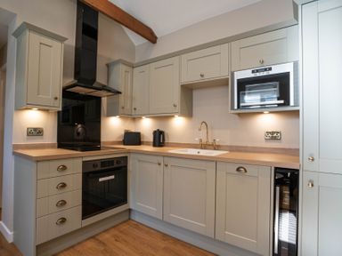 A kitchen with gray cabinets wooden countertop oven microwave and sink at Dunes Cottage in Kessingland