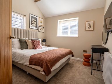 A bedroom with a bed with pillows and a brown blanket and framed pictures on the walls at Dunes Cottage in Kessingland