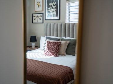 A bedroom with a bed with multiple pillows a brown blanket a nightstand with a lamp and wall art at Dunes Cottage in Kessingland