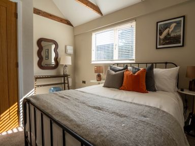A bedroom with a bed with multiple pillows a wooden door a mirror on the wall and a window at Dunes Cottage in Kessingland
