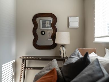 A corner with a wooden table holding a lamp and a wavy framed mirror on the wall at Dunes Cottage in Kessingland