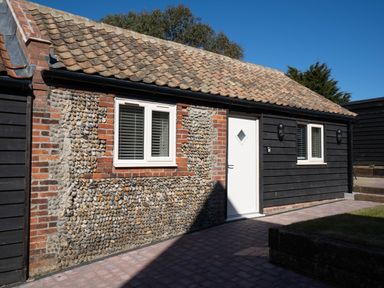 A building exterior with tiled roof white doors and windows and pebble and brick walls at Dunes Cottage in Kessingland