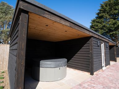 An outdoor wooden structure with a covered hot tub and paved floor at Dunes Cottage in Kessingland
