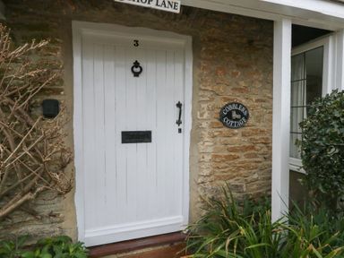 A white door with the number 3 and a black door knocker on a stone cottage wall with a sign reading Cobblers Cottage Langton Herring