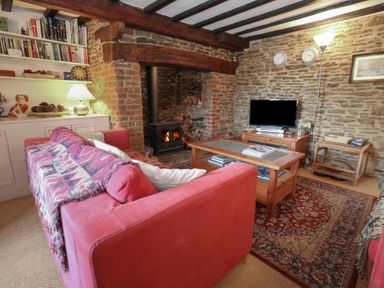A living room with a red sofa a fireplace a wooden coffee table and a television at Cobblers Cottage in Langton Herring