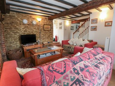 A living room with red sofas a wooden coffee table a TV on a wooden stand and a staircase at Cobblers Cottage in Langton Herring