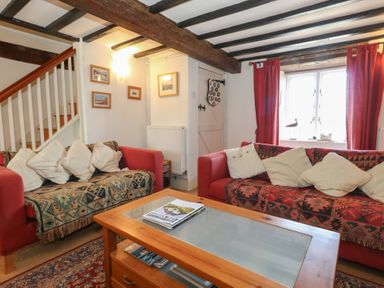 A living room with two sofas and a wooden coffee table near a window with red curtains at Cobblers Cottage in Langton Herring
