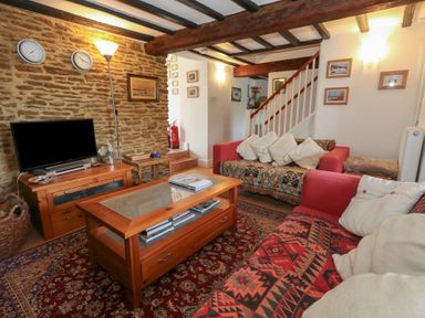 A living room with sofas cushions a coffee table a television on a stand and exposed wooden beams at Cobblers Cottage in Langton Herring