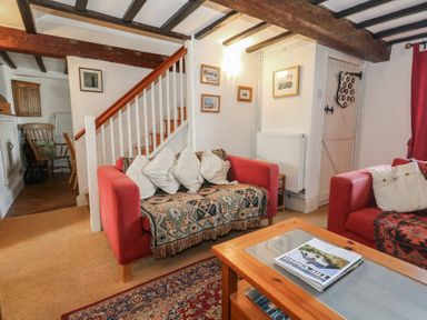 A living room with red sofas white pillows wooden staircase and a coffee table at Cobblers Cottage in Langton Herring