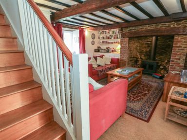 A living room with wooden stairs a wood stove and red sofas at Cobblers Cottage in Langton Herring