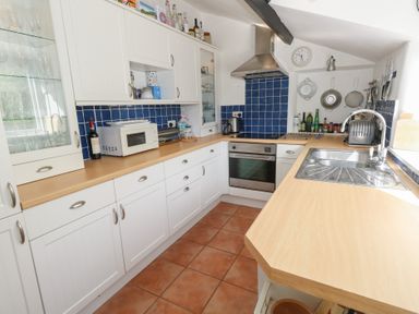 A kitchen with white cabinets wooden countertops a microwave sink stove and blue tiled backsplash at Cobblers Cottage in Langton Herring