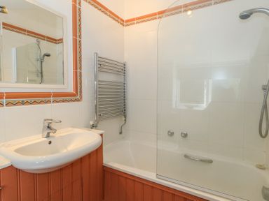 A bathroom with a sink a mirror a bathtub with a glass shower screen and a towel radiator at Cobblers Cottage in Langton Herring