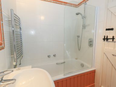 A bathroom with a bathtub shower combination a sink a heated towel rail and a wooden door at Cobblers Cottage in Langton Herring