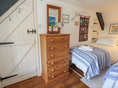 A bedroom with a wooden chest of drawers a mirror a bed with blue striped bedding and a white wooden door at Cobblers Cottage in Langton Herring